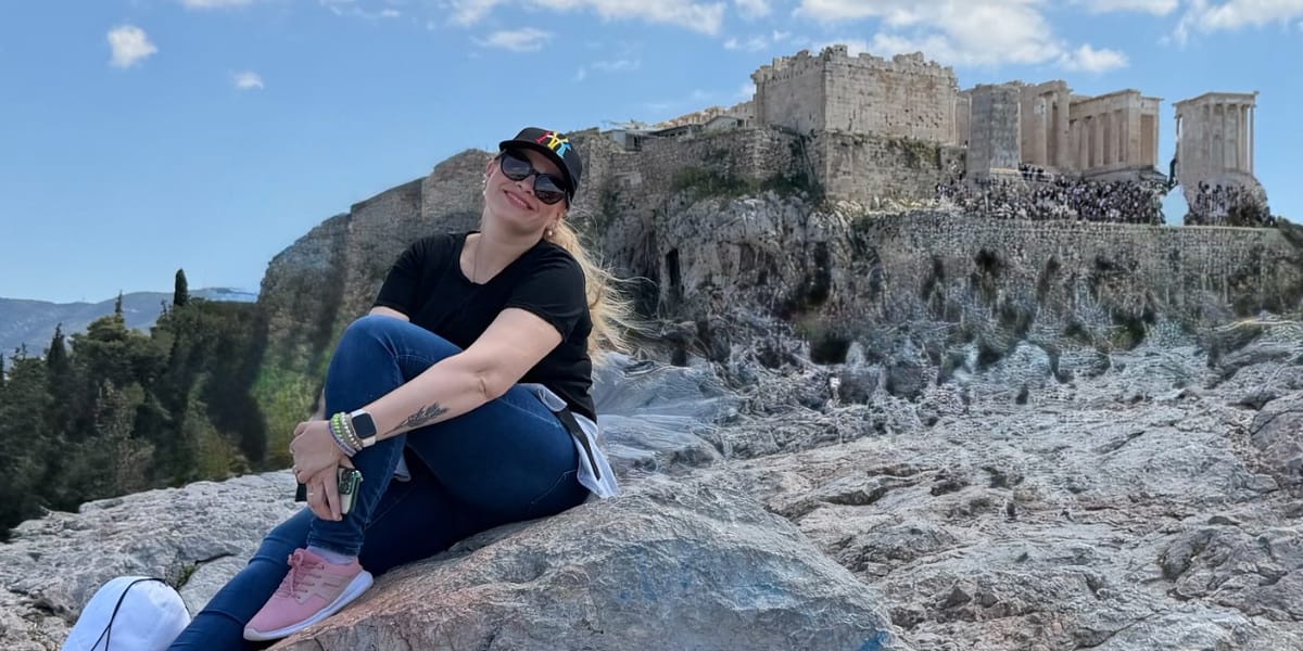 Lesia sentada en una roca, con la Acrópolis al fondo